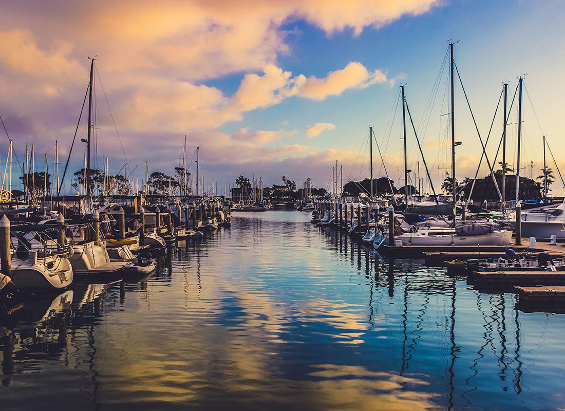 About Our Agency - Two Rows of Boats Docked on the Harbor at Sunset with Cloud Reflections in the Water