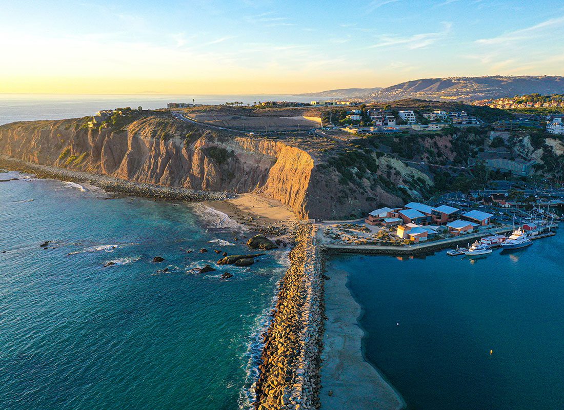 Capistrano Beach, CA - View of Seawall and Coast with Turquoise Blue Waters Against a Sunset Sky in Capistrano Beach California