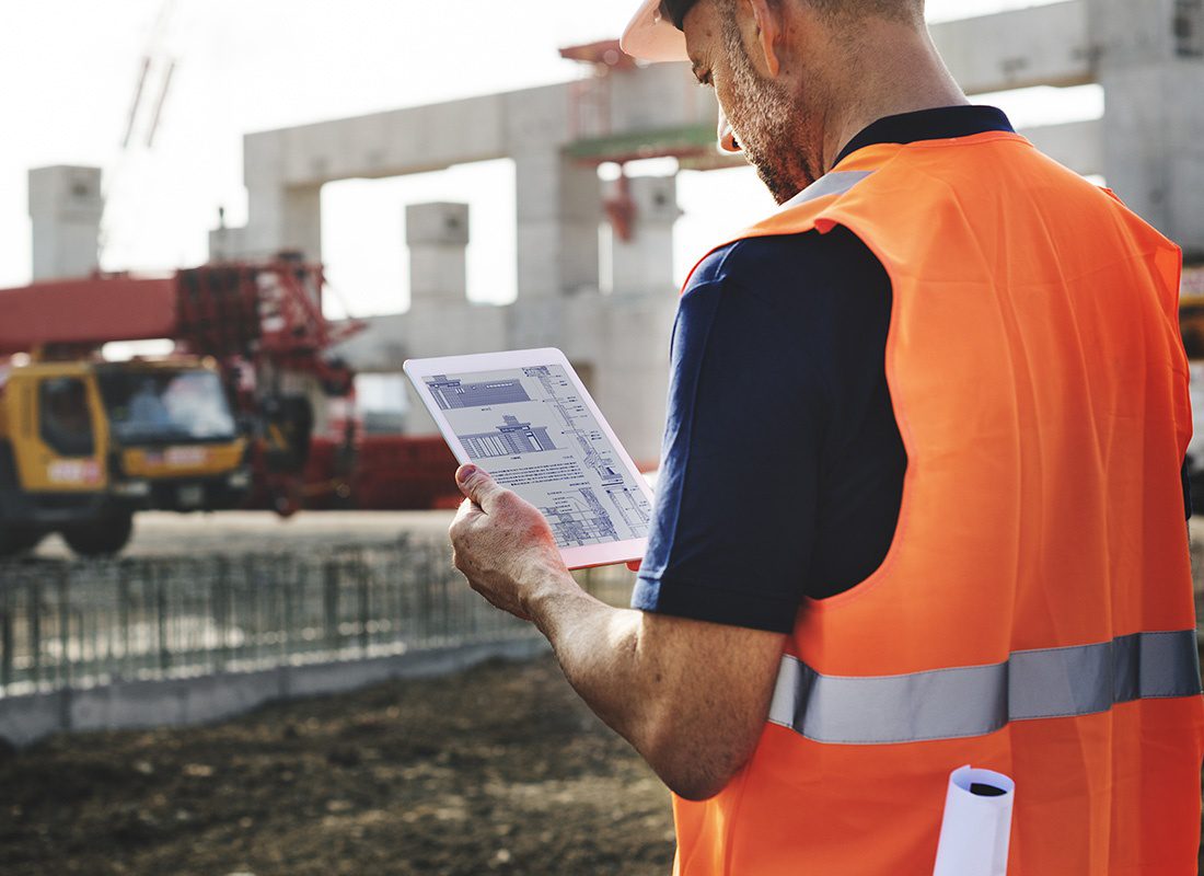 Business Insurance - Closeup Portrait of a Contractor Checking Blueprints on a Tablet While Standing on a Commercial Construction Jobsite